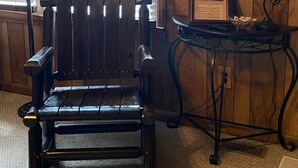 A wooden chair with a metal frame, a small table with a lamp, and a wall-mounted thermometer. - A & B TRAIL HOUSE @ Hatfield-McCoy Trails, 5 Beds Plus Futon 2 Couches & 2 Baths (DELBARTON)