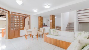 A modern living room with a sofa, dining table, chairs, and a kitchen area in the background.