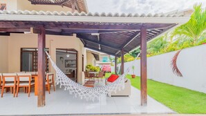 A covered patio with a hammock, outdoor dining area, and a view of the adjacent house.