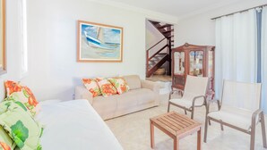 A living room with a sofa, chairs, a coffee table, a painting, and a staircase.