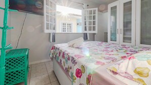 A room with a bed, an open window, a green chair, and a wardrobe.