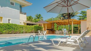 A pool area with lounge chairs, a pergola, and a barbecue setup.