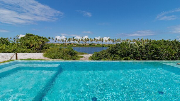 A clear blue pool with a view of a beach and palm trees.