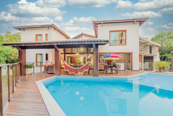 Une maison à deux étages avec une piscine, un espace salon extérieur et un hamac.