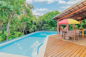 Une piscine dotée d’une terrasse en bois, entourée d’une végétation luxuriante.
