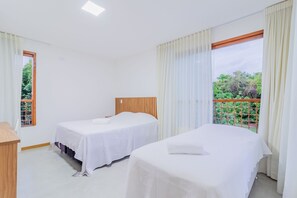 Une chambre d’hôtel avec deux lits simples, une tête de lit en bois, un petit bureau et une fenêtre avec des rideaux.