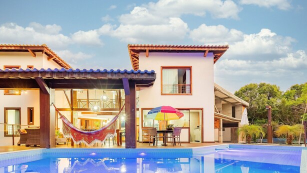 Una casa moderna con piscina, un'amaca e un'area pranzo con ombrellone.