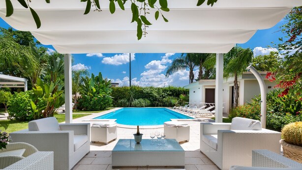 Un espace extérieur abrité, doté d’une piscine, de meubles en osier blancs et d’une végétation luxuriante.