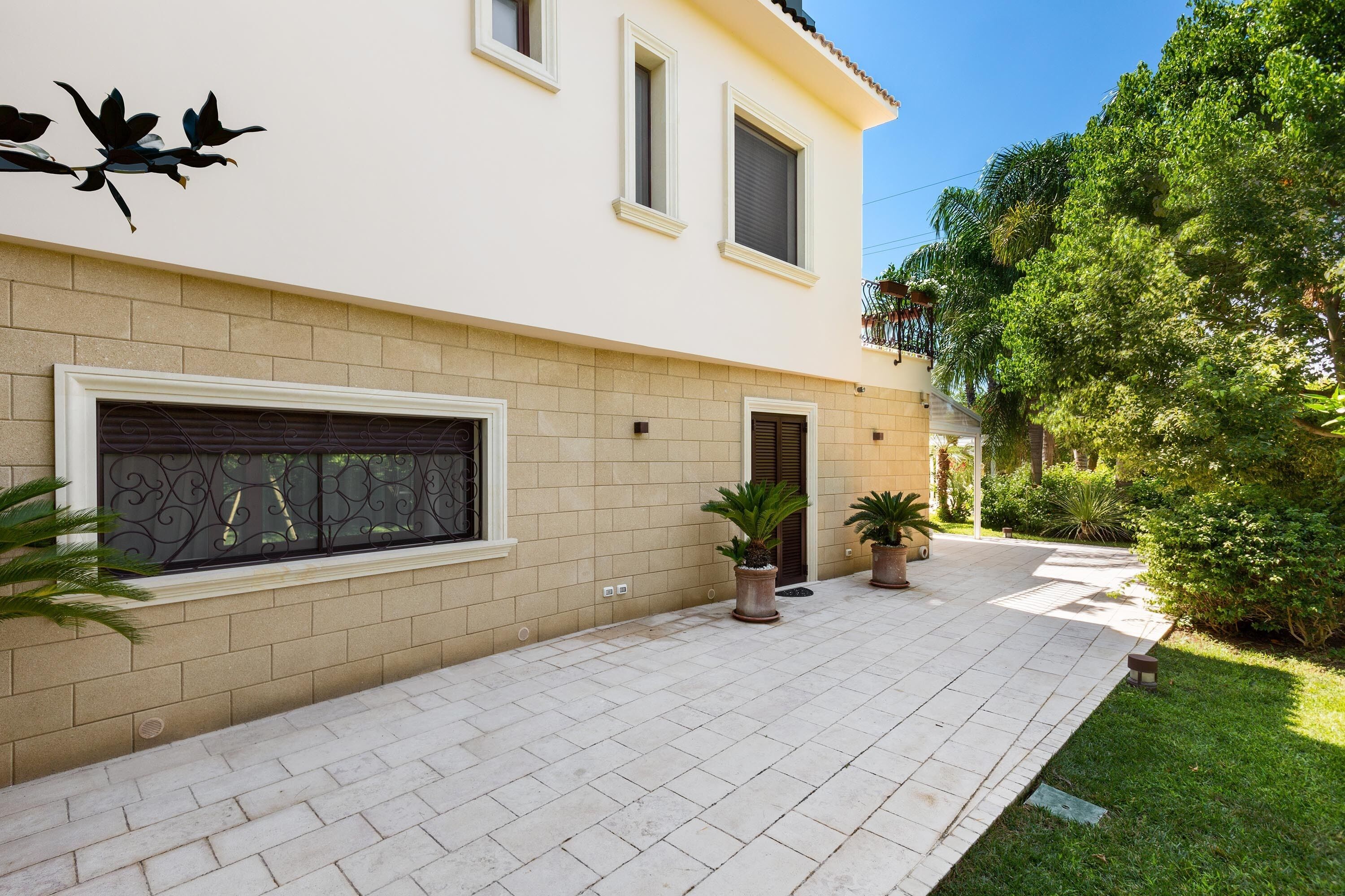 Una casa moderna con patio piastrellato, piante in vaso e una scultura decorativa a forma di uccello.