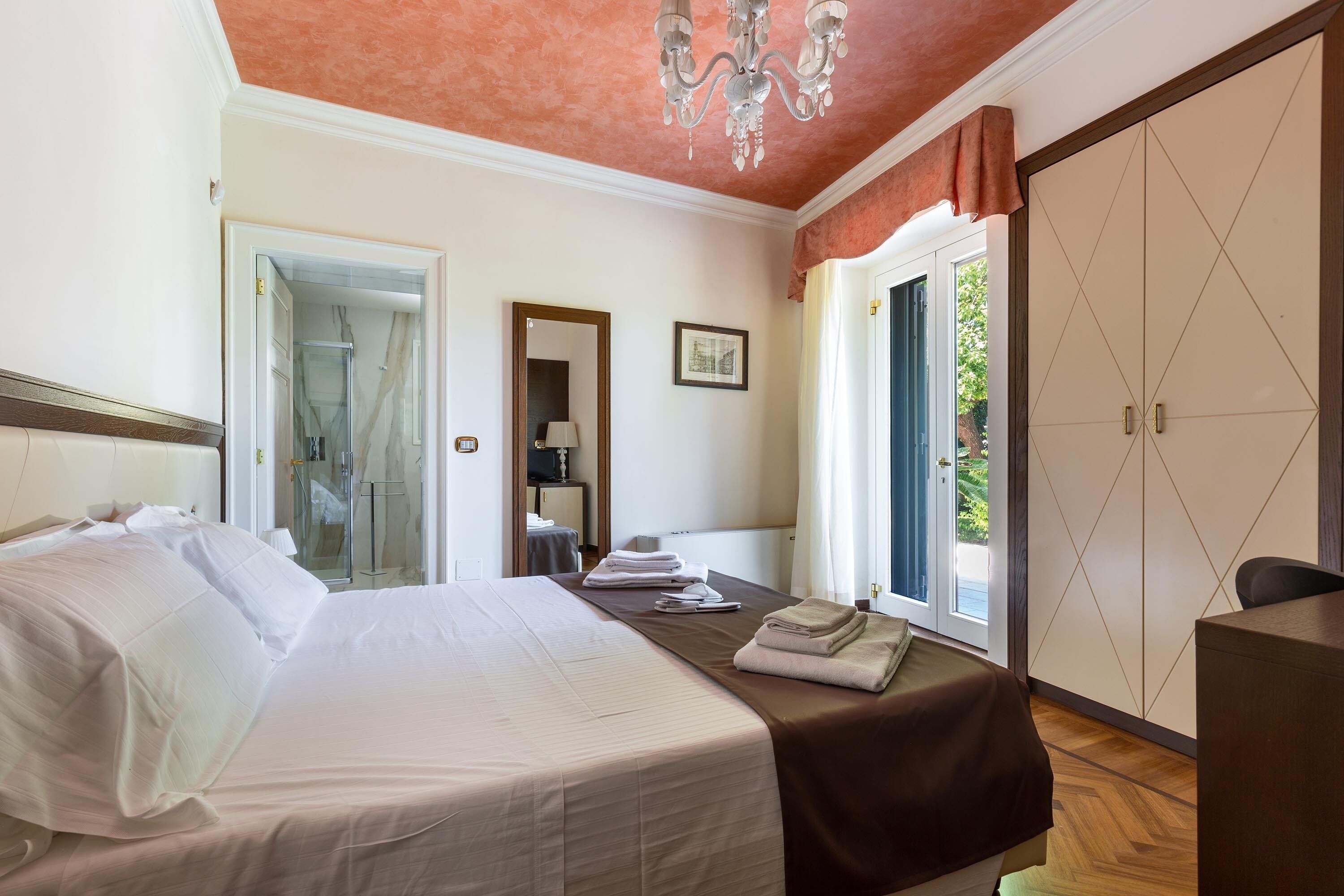A hotel room with a bed, a desk, a wardrobe, and a bathroom visible through an open door.
