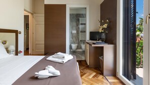 Une chambre d’hôtel avec un lit, un bureau avec un ordinateur, une salle de bain visible à travers une porte ouverte et une vue sur l’extérieur.