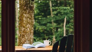 A view through a window with a wooden table, a chair, and a book. - Mt Snow Chalet: Peaceful Escape w/Hot Tub (Wilmington)