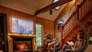 A cozy living room with a fireplace, a television, a comfortable seating area, and a staircase. - Mt Snow Chalet: Peaceful Escape w/Hot Tub (Wilmington)