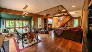 A spacious living area with a dining table, chairs, a fireplace, and a staircase leading to a loft. - Mt Snow Chalet: Peaceful Escape w/Hot Tub (Wilmington)