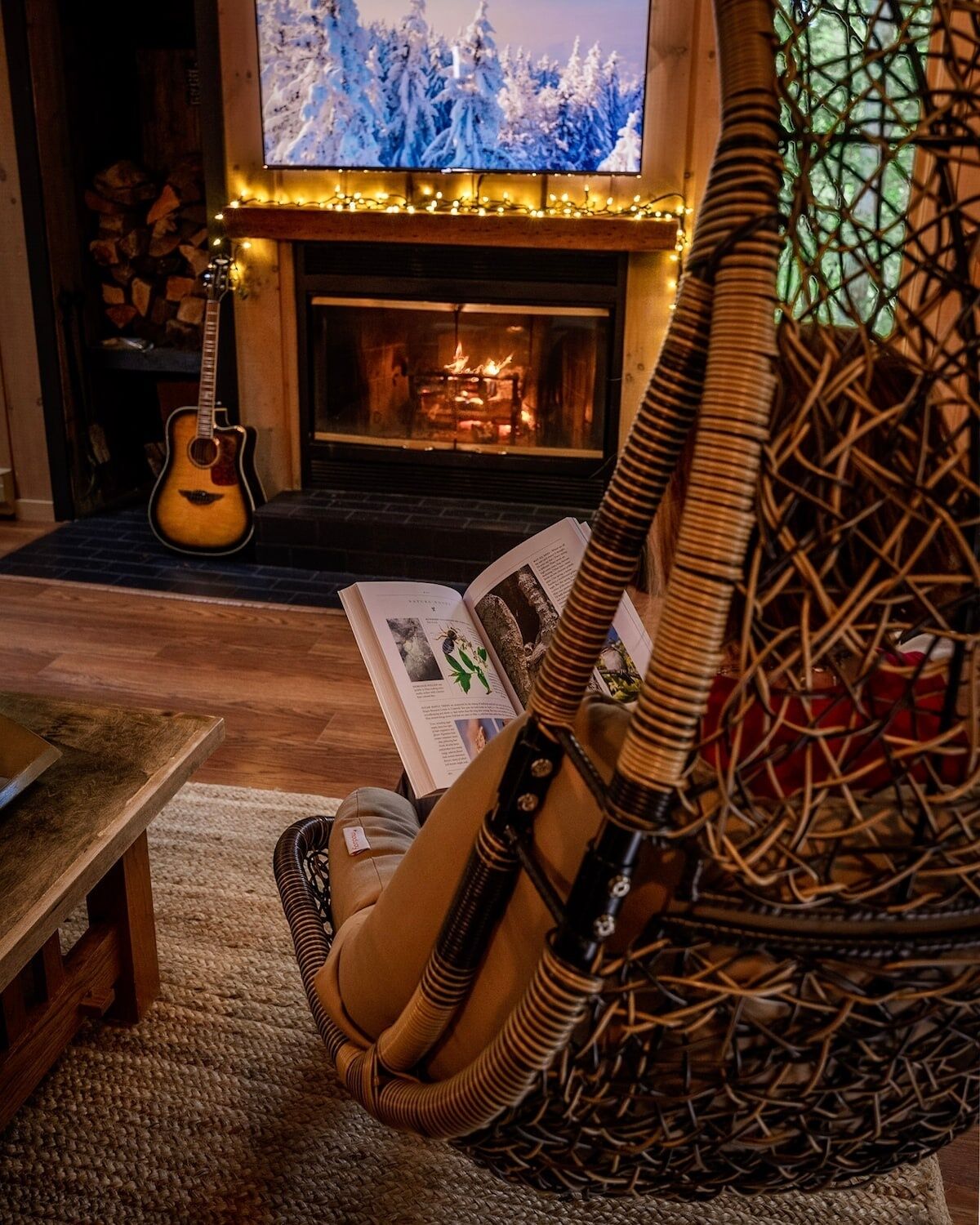 A cozy living room with a fireplace, a guitar, and a wicker chair.