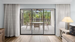 Een kamer met een schuifdeur naar een terras buiten, met een tafel en stoelen, een lamp op een bijzettafeltje, en een houten vloer.