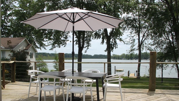 A wooden deck with a table and chairs, an umbrella, and a view of a lake.