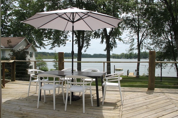 Une terrasse en bois avec une table et des chaises, un parasol et une vue sur un lac.
