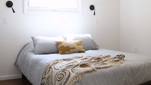 A bedroom with a bed, a ceiling fan, a window, and wall-mounted lights.