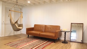 A room with a hanging chair, a brown sofa, a patterned rug, and a round table with candles.