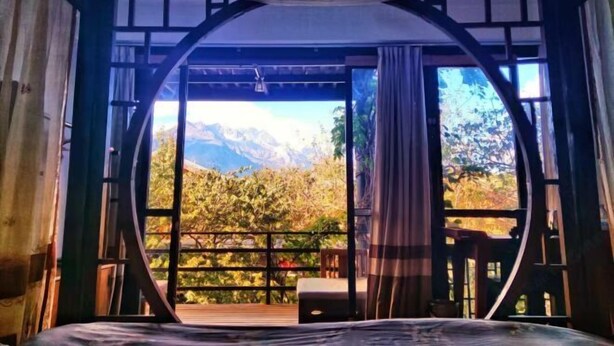 A room with a bed, a wooden deck, and a view of mountains and trees. - Ziyou Suiyue Design Hostel (Yulong)