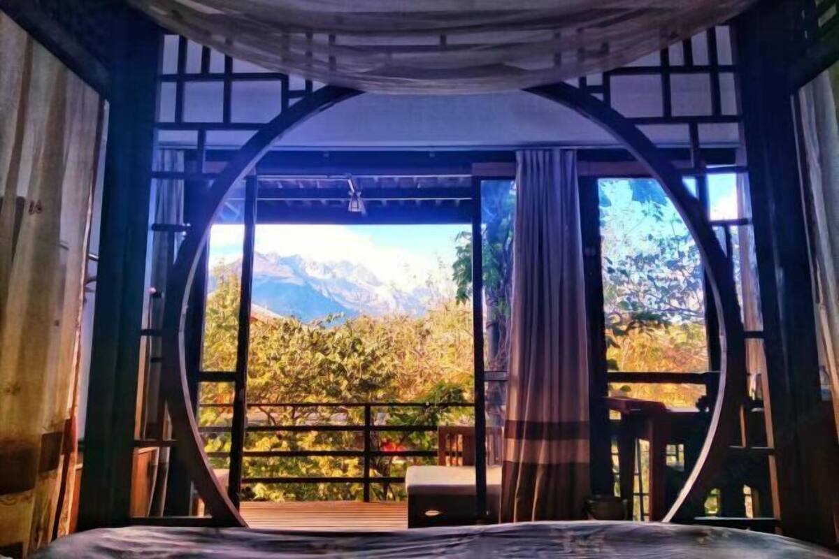 A room with a bed, a wooden deck, and a view of mountains and trees.