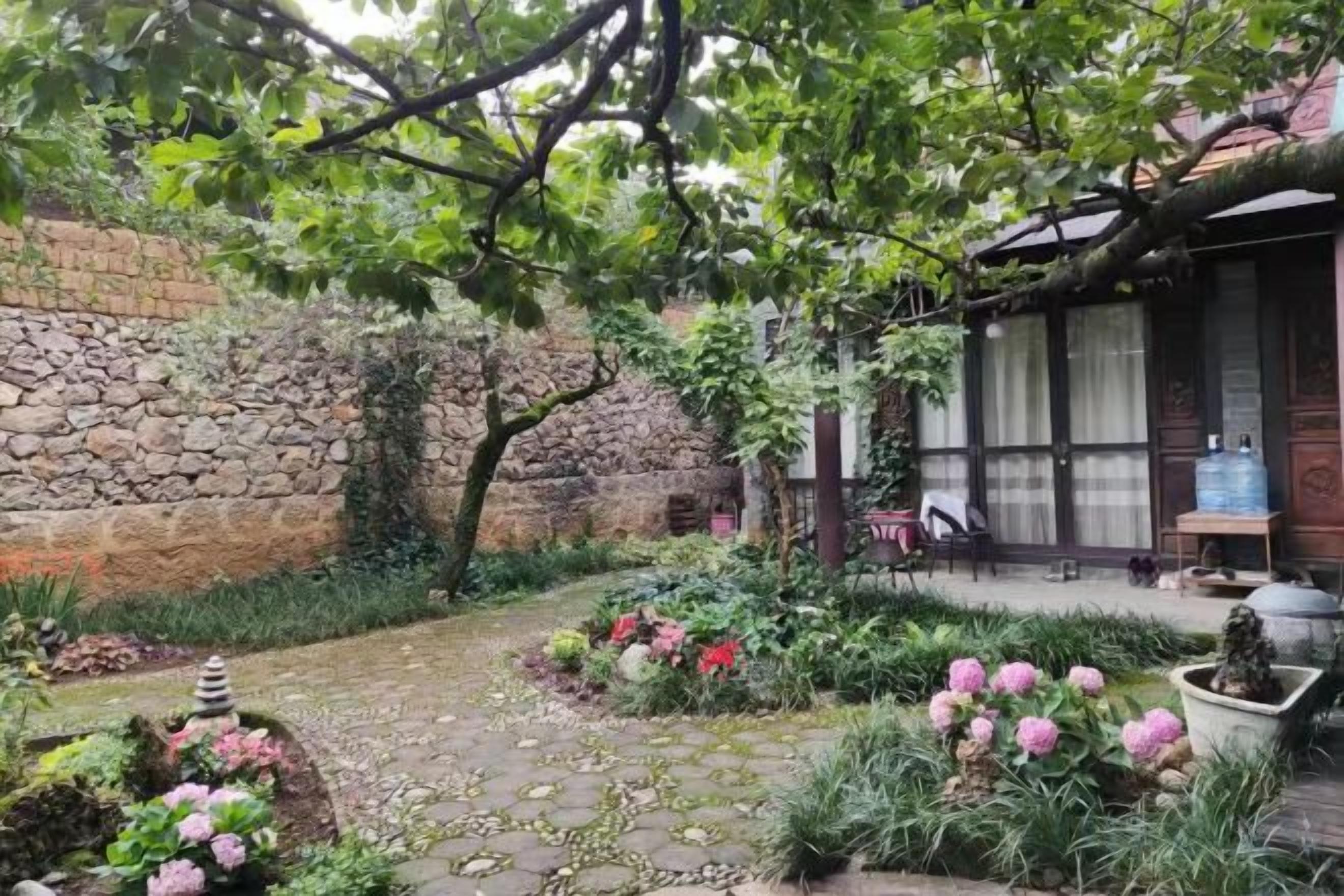 A garden with a stone wall, potted plants, and a wooden structure.