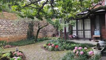 A garden with a stone wall, potted plants, and a wooden structure.