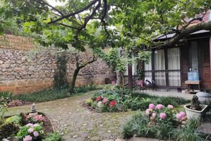 A garden with a stone wall, potted plants, and a wooden structure. - Ziyou Suiyue Design Hostel (Yulong)