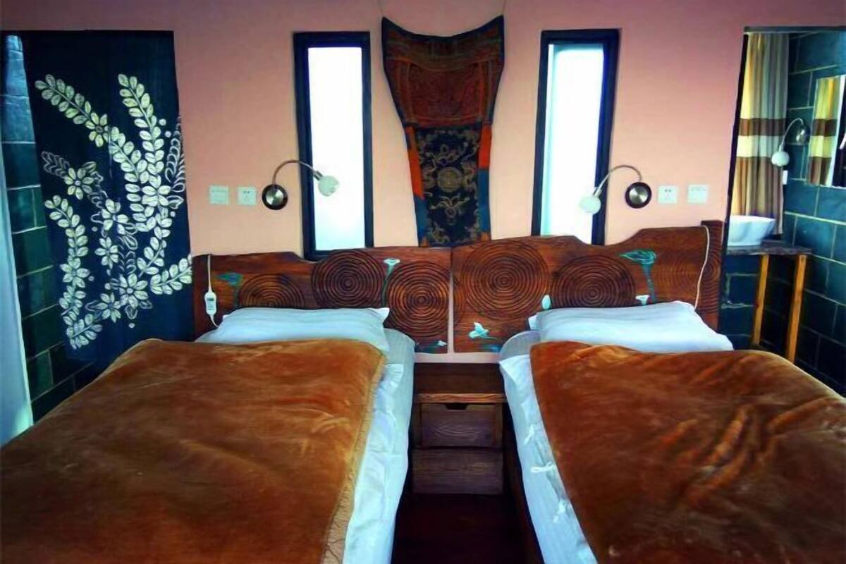 A room with two beds, a window, a wall tapestry, and a mirror.