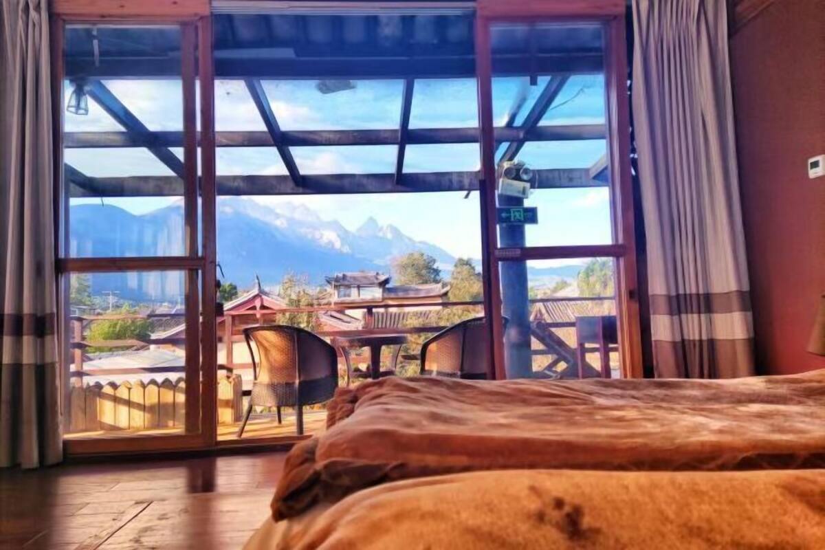 A room with a bed, a view of mountains, and a balcony with chairs and a table.