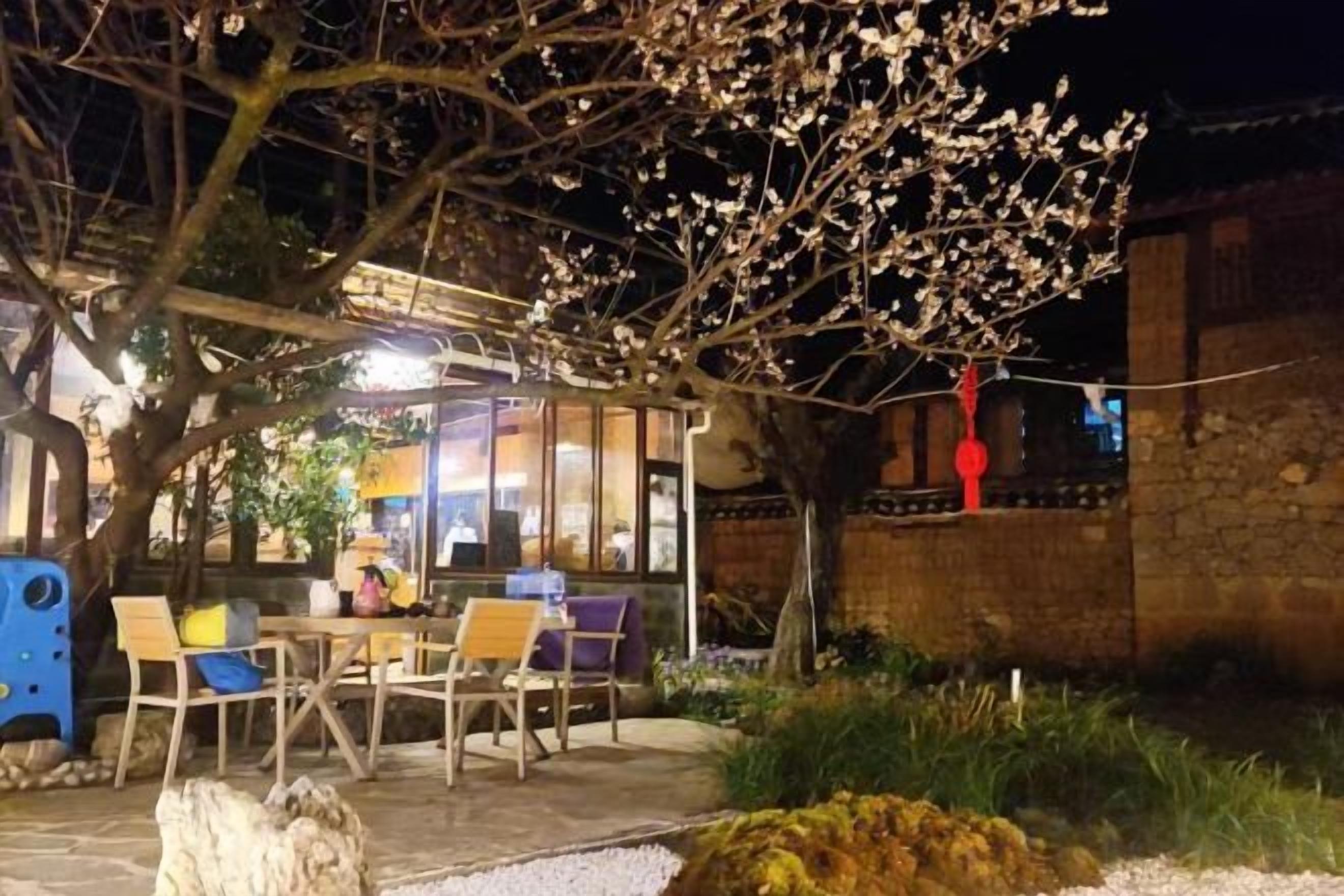 An outdoor seating area with tables and chairs, a stone wall, and a tree with blossoms.