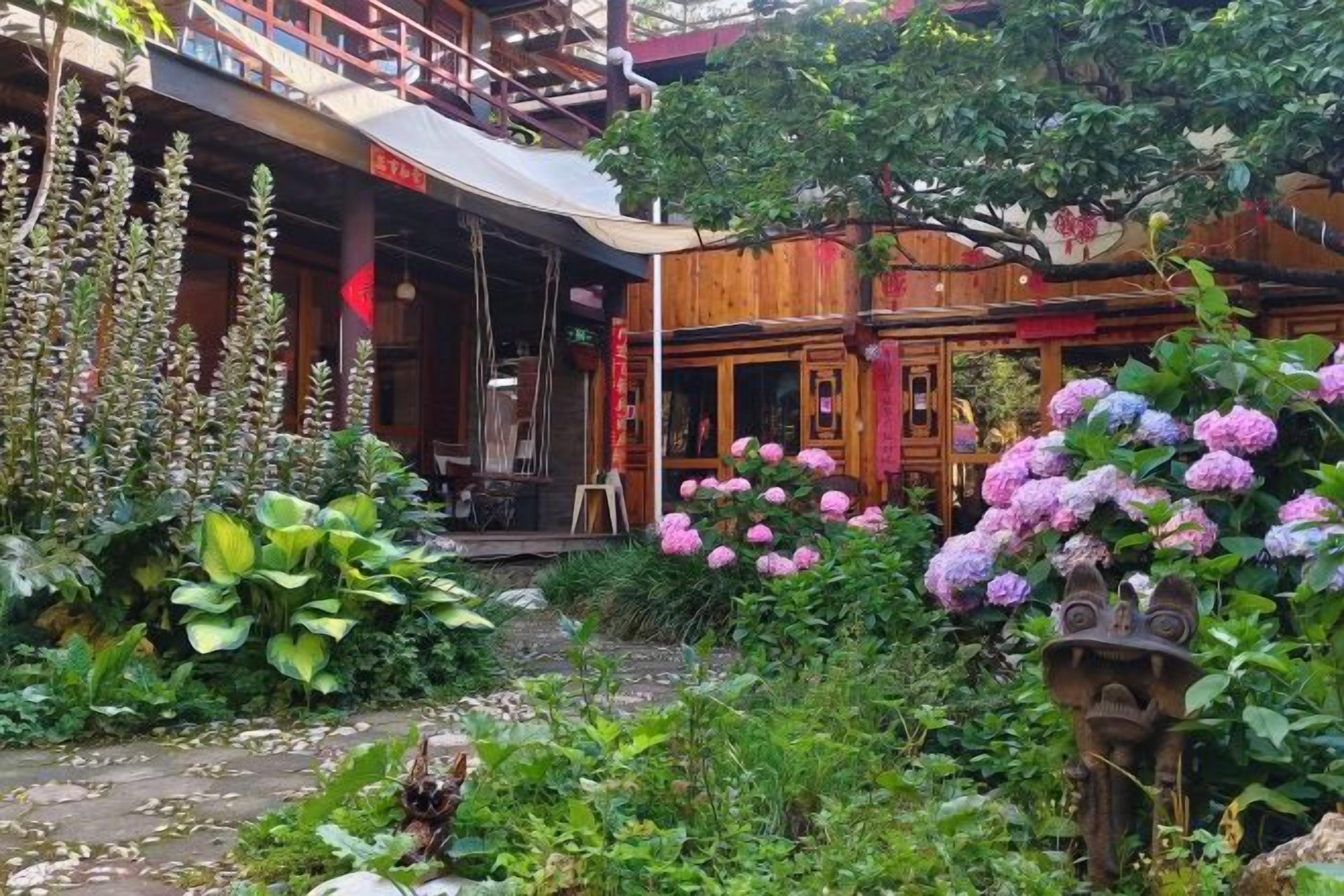 A traditional wooden building with a covered outdoor seating area, surrounded by lush greenery and flowering plants.