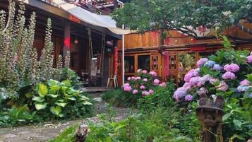 A traditional wooden building with a covered outdoor seating area, surrounded by lush greenery and flowering plants.
