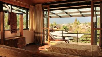 A wooden room with a bed, a bench, and a view of houses through large windows.