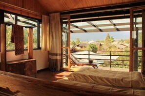 Une pièce en bois avec un lit, un banc et une vue sur les maisons à travers de grandes fenêtres.