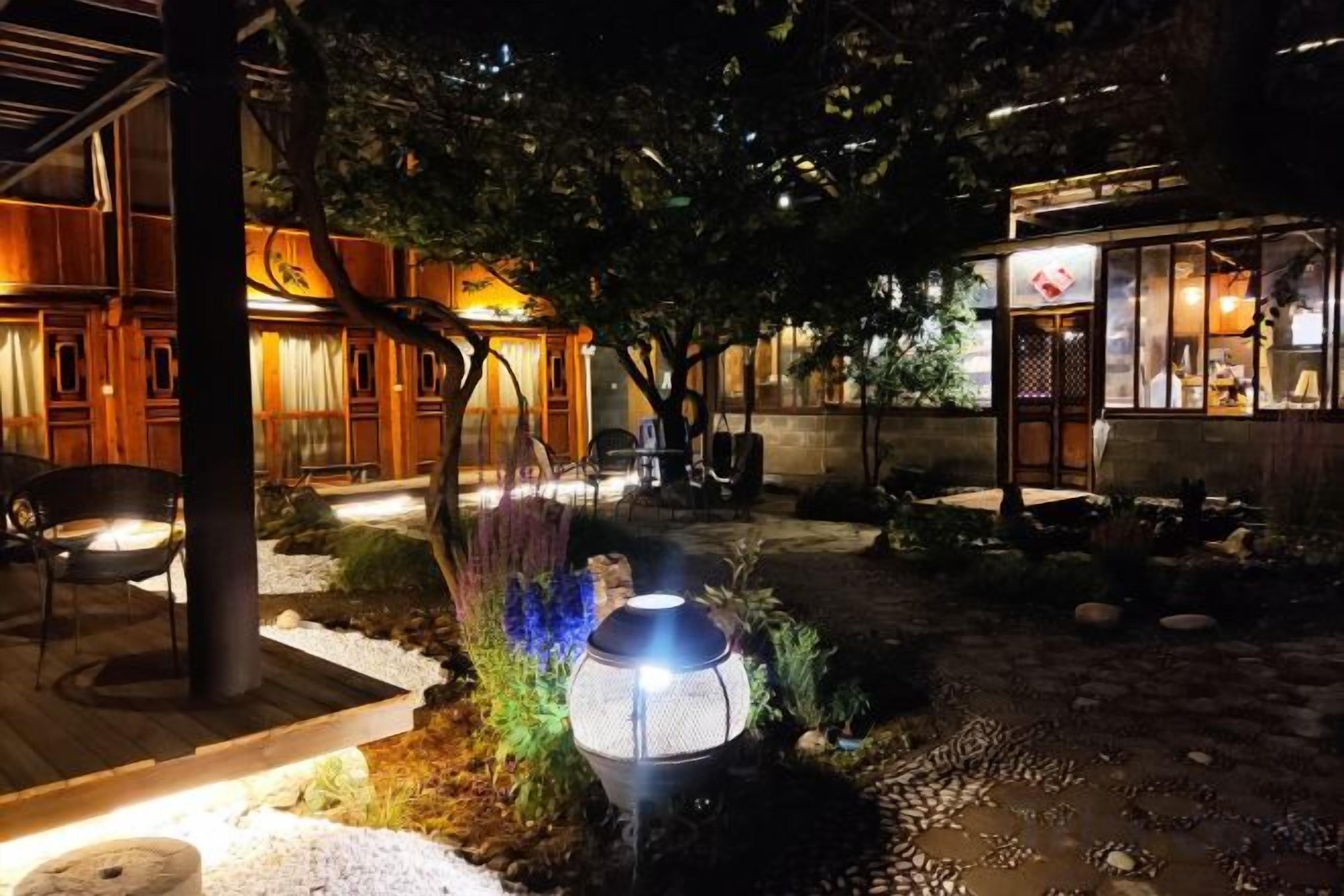 A courtyard with a traditional wooden building, a seating area, and a small structure with a sign.