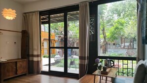 A room with a sliding glass door to an outdoor area, a wooden cabinet, a small table with a vase, and a sofa. - Ziyou Suiyue Design Hostel (Yulong)