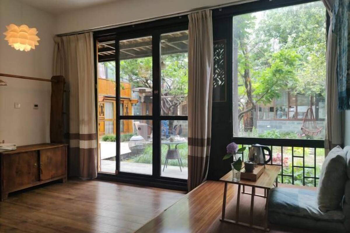 A room with a sliding glass door to an outdoor area, a wooden cabinet, a small table with a vase, and a sofa.