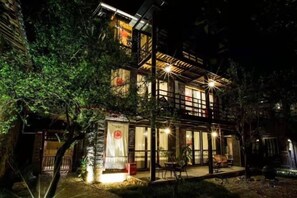 A two-story building with a balcony, illuminated by exterior lighting, surrounded by trees. - Ziyou Suiyue Design Hostel (Yulong)