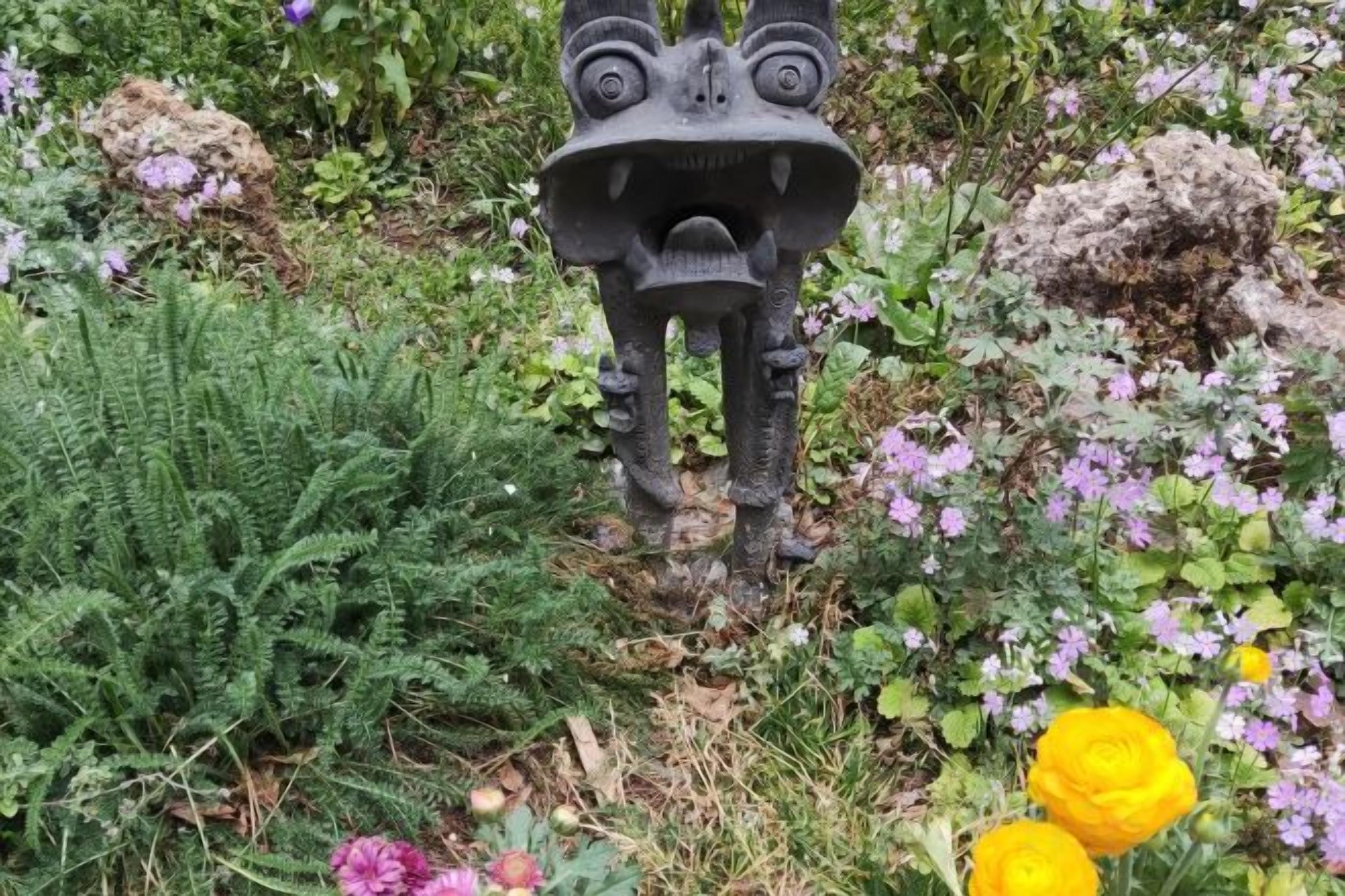 A garden with a stone statue, ferns, and purple flowers.