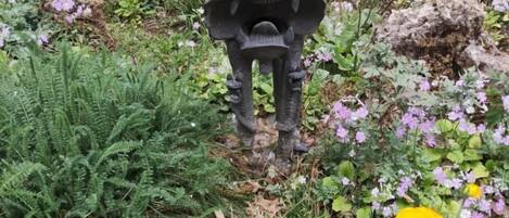 A garden with a stone statue, ferns, and purple flowers.