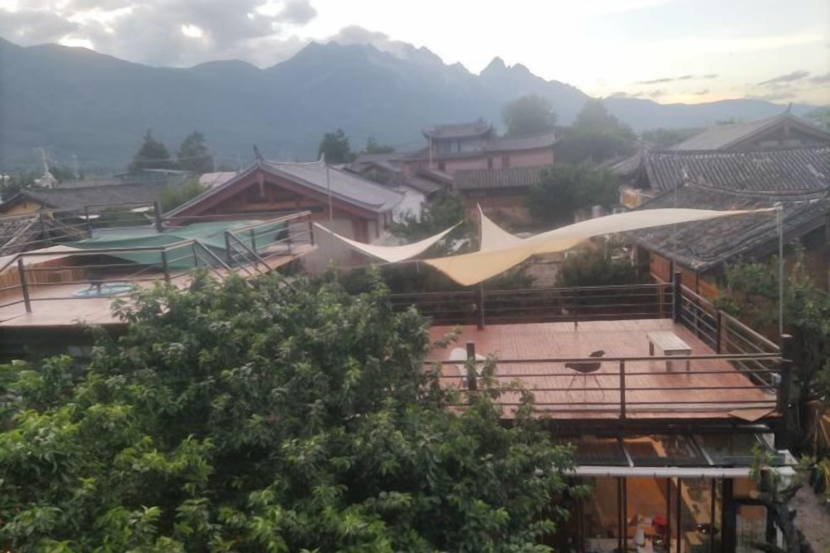 A traditional building with a rooftop terrace, surrounded by greenery and mountains in the background.