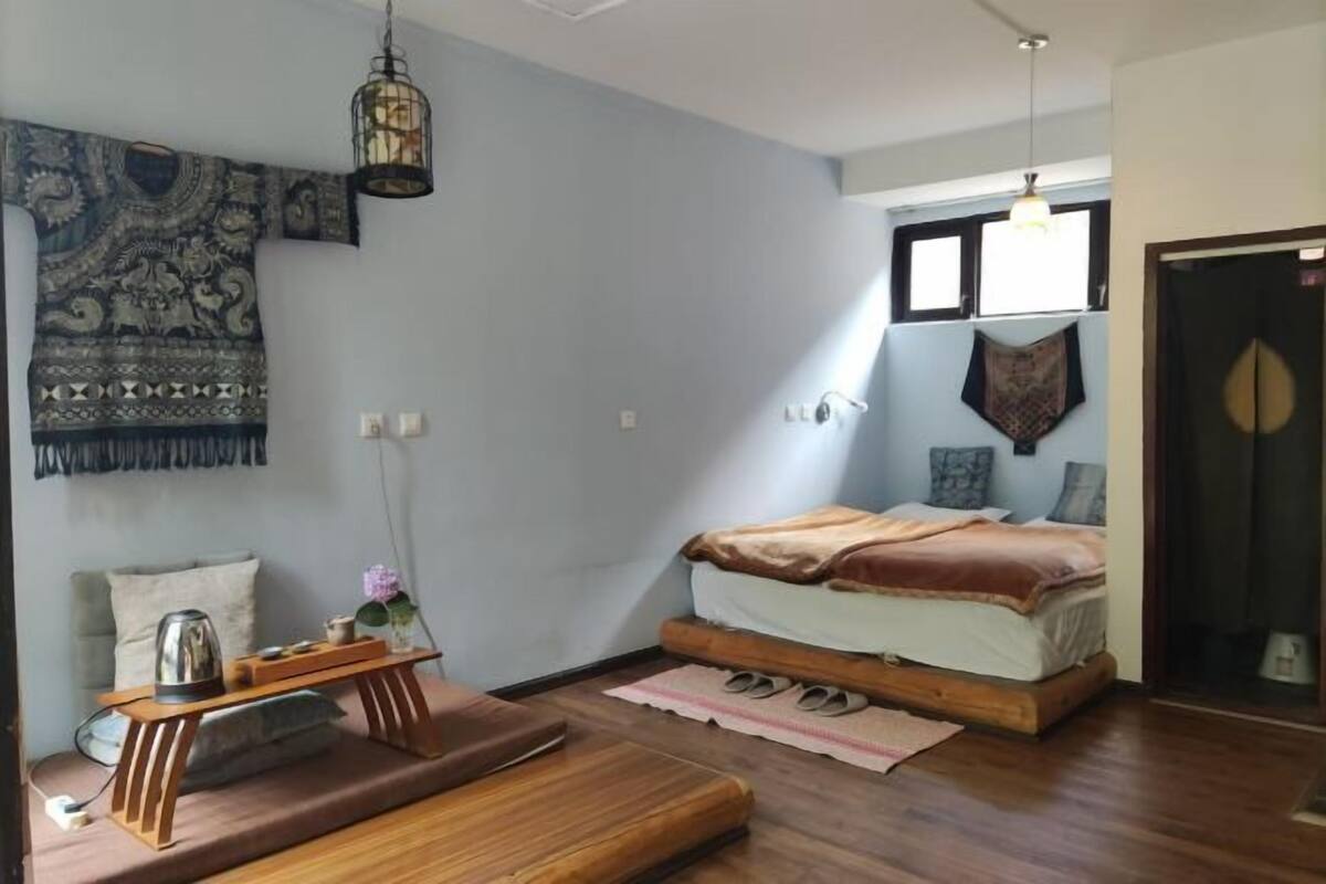 A room with a bed, a small table, a wall tapestry, and a hanging light fixture.