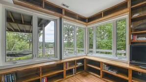 A corner seating area with built-in bookshelves and large windows offering a view of greenery. - Stepping Stone Cove :: Lakefront w/ Dock, Fireplaces & Hot Tub (Mineral)
