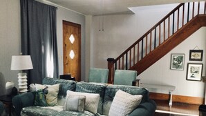 Una sala de estar con un sofá verde, una escalera de madera y cuadros en la pared.