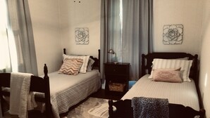 Un dormitorio con dos camas individuales, una mesita de noche, una silla y un tapete estampado.