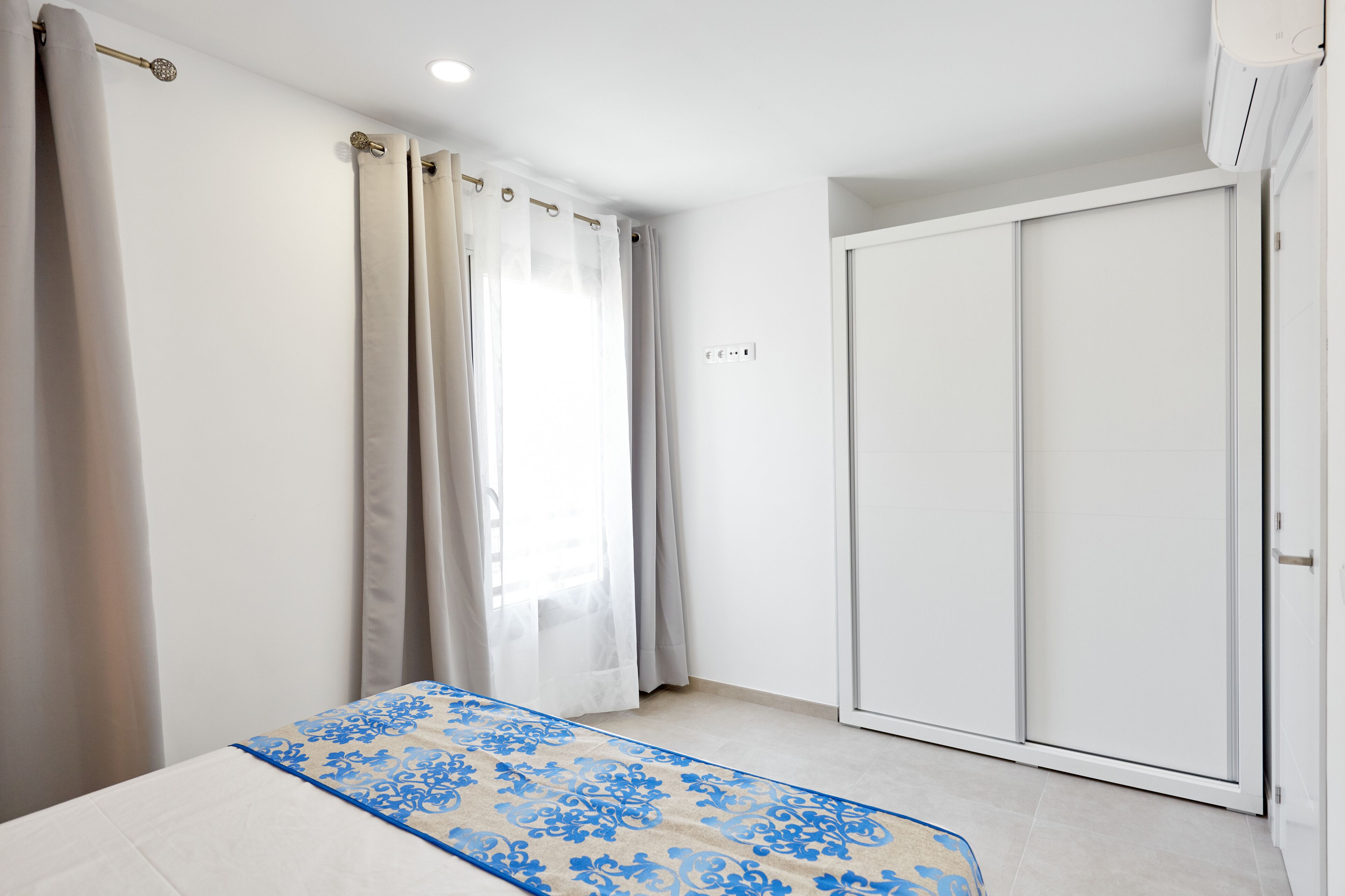 A bedroom with a bed, a wardrobe, and a window with curtains.
