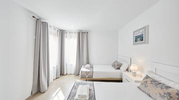 A modern hotel room with a large bed, a smaller bed, a nightstand with a lamp, and a framed picture on the wall.