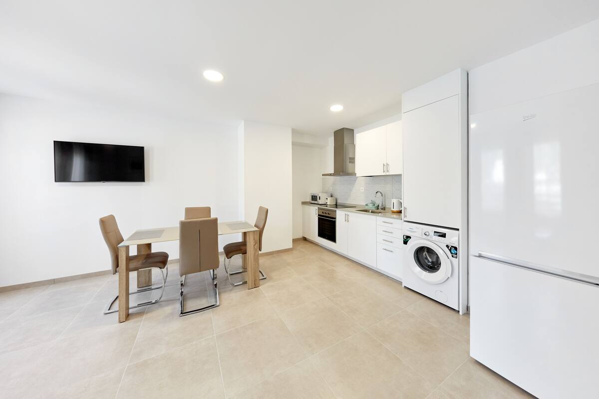 Een moderne keuken met een eethoek, een wasmachine en een flatscreen televisie.